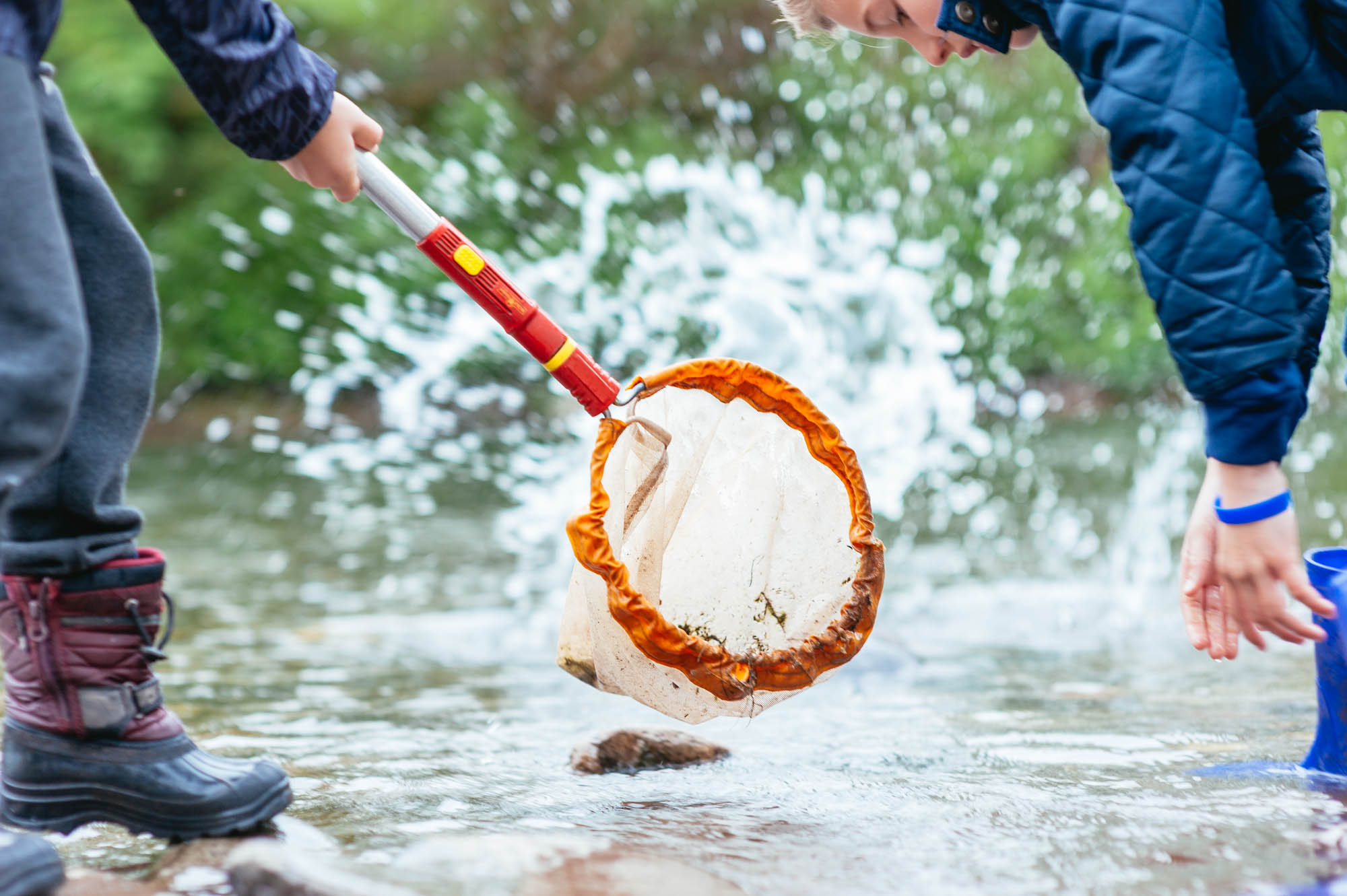 Two children investigating the river water with a red net