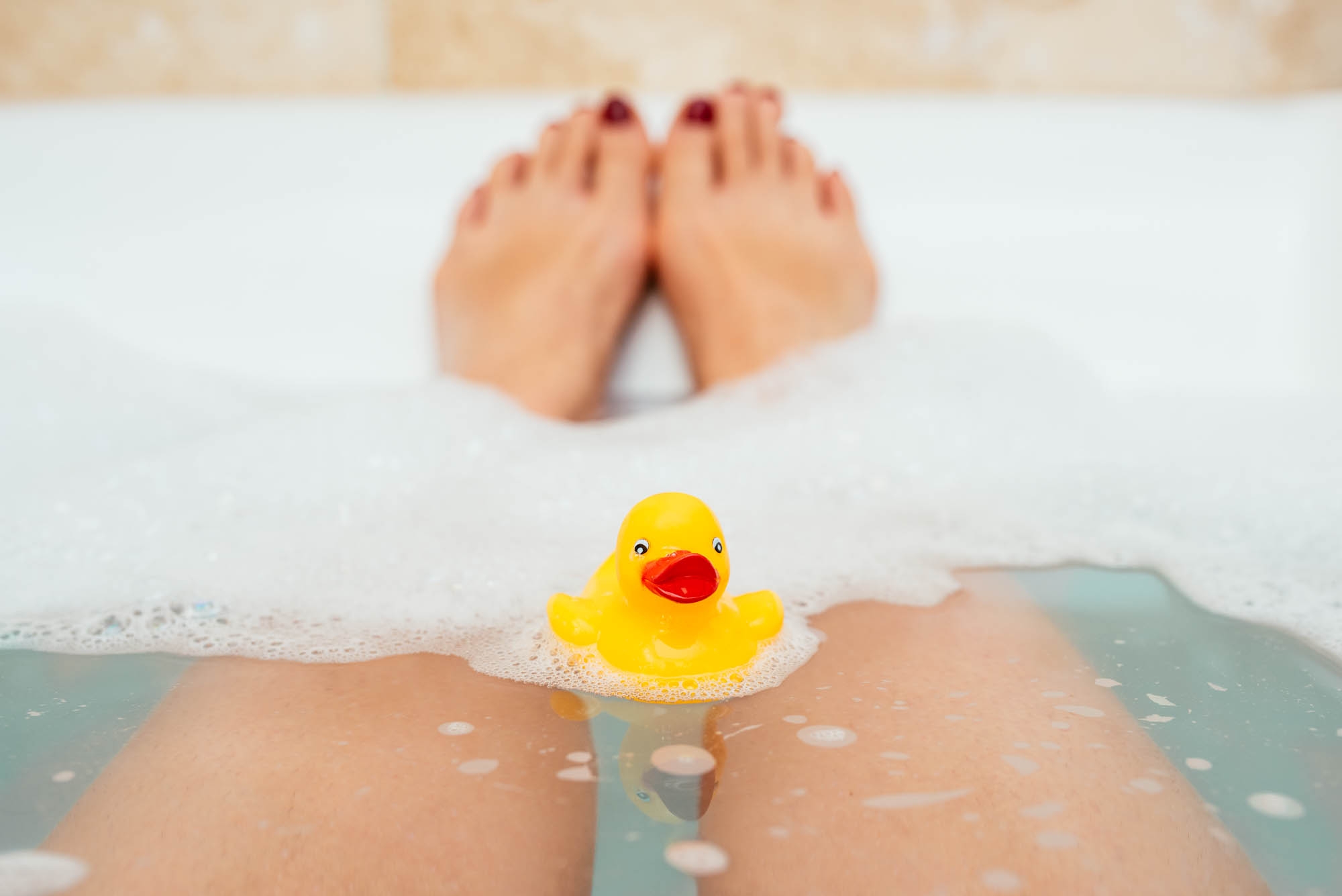 A Photo of a yellow duck floating in a bathtub with feet rising up